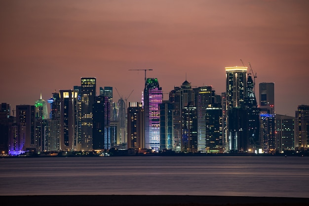 Vibrante Skyline di Doha di notte visto dal lato opposto del tramonto della baia della città capitale.