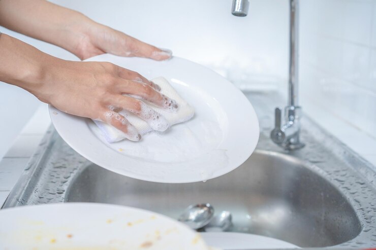 Vicino alla femmina asiatica lava il piatto in cucina con la sua spugna per lavare i piatti