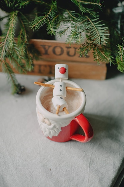vicino alla scatola con albero di Natale verde una coppa a forma di Babbo Natale con cacao e pupazzo di neve f