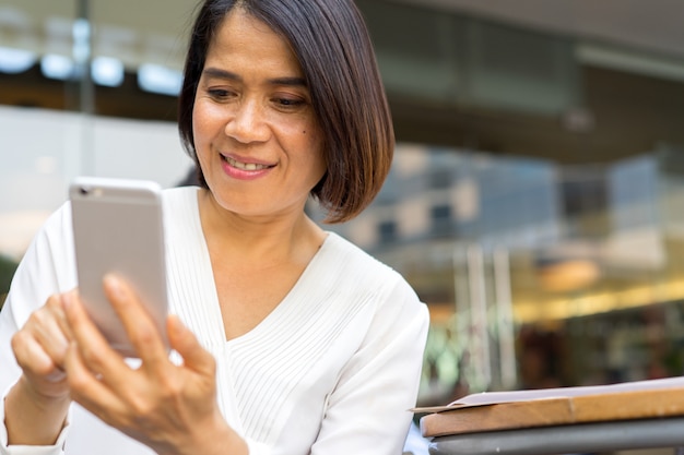 vicino donna matura che tiene smartphone e controllo notizie, persone e tecnologia