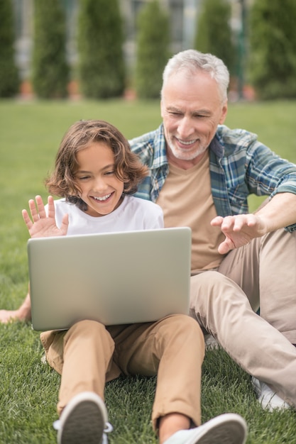 Video chiamata. Figlio e papà seduti insieme a un laptop e facendo una videochiamata