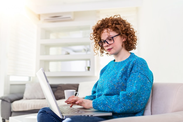 Video di sorveglianza delle free lance della giovane donna positiva in blog su netbook e che mangiano un caffè a casa comoda. Bella giovane donna di affari che lavora al computer portatile. Freelancer che si collega ad Internet