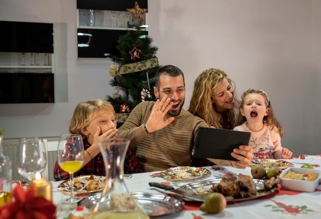 Videochiamata di famiglia caucasica da tablet durante la cena di Natale Padre madre figlio e figlia che salutano