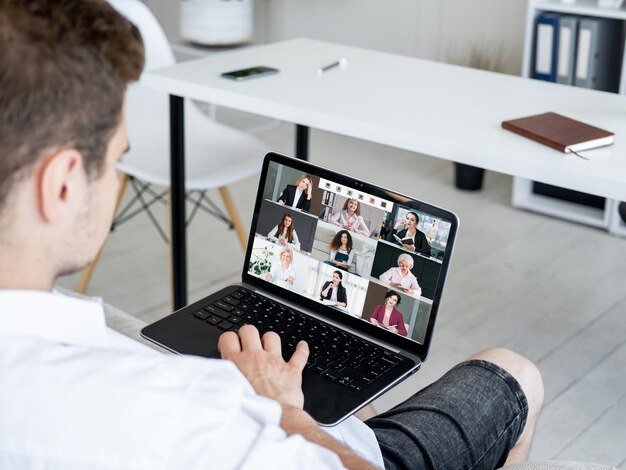 Videochiamata di gruppo Riunione remota Wfh telelavoro Uomo rilassato che utilizza il laptop che lavora da casa online con il team di lavoro femminile sullo schermo