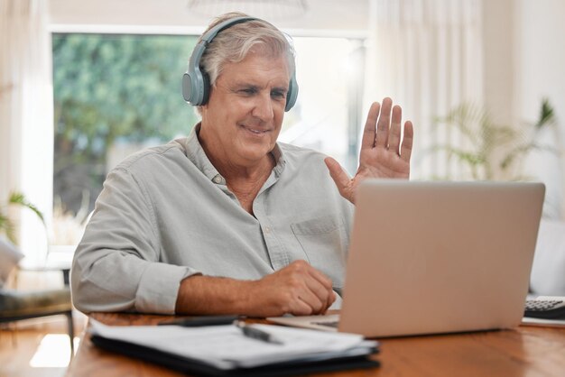 Videochiamata portatile e onda con un uomo d'affari senior che chatta online con le cuffie e un computer a casa Internet per conferenze e comunicazione con un dipendente maschio maturo che lavora a distanza