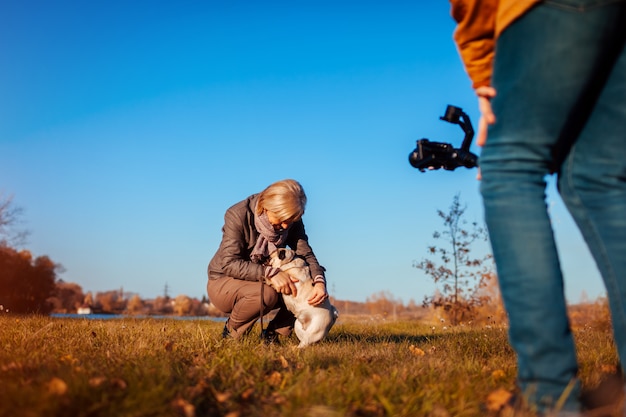 Videografo riprese donna con cane nel parco in autunno Uomo che usando steadicam e macchina fotografica per fare filmati