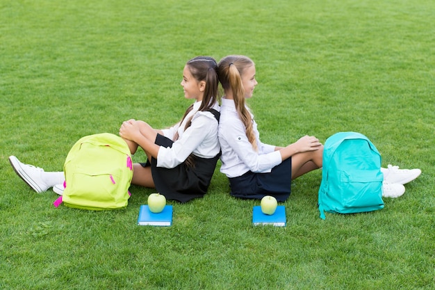 Vieni, rilassati e divertiti. Le ragazze della scuola si siedono sull'erba verde. Le ragazze felici indossano l'uniforme scolastica. Di nuovo a scuola. Sguardo di bellezza delle bambine. Piccole ragazze in trecce. Parrucchiere. La bellezza sta nella mente sana.