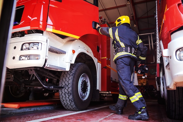 Vigile del fuoco che apre la porta del camion dei pompieri ed entra nella stazione dei vigili del fuoco. È preparato per l'azione.