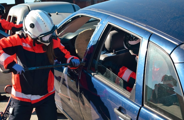 Vigile del fuoco femminile davanti a un'auto schiantata che cerca di aprire la porta con un rampino