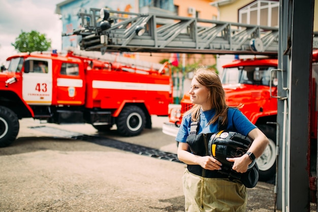 Vigile del fuoco femminile in uniforme protettiva in piedi vicino al camion dei pompieri rosso