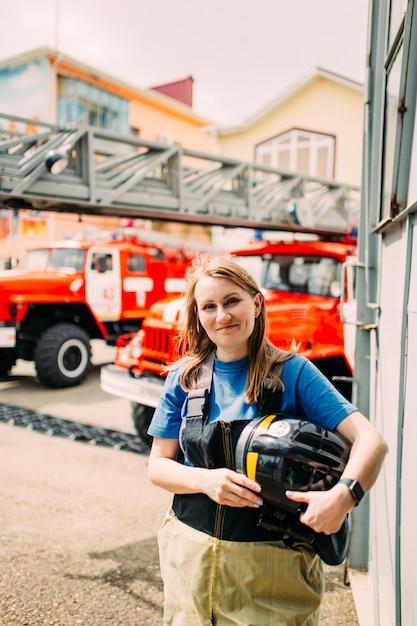 Vigile del fuoco femminile in uniforme protettiva in piedi vicino al camion dei pompieri rosso