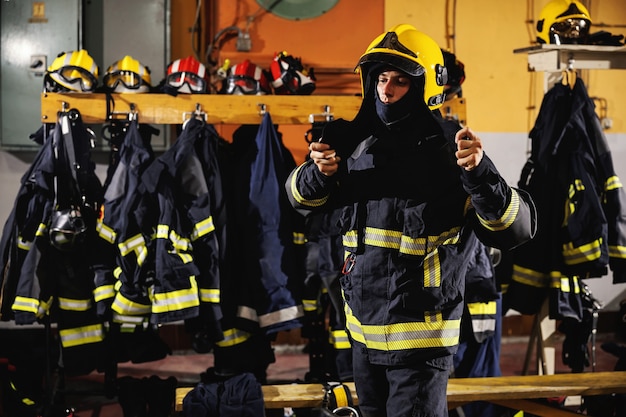 Vigile del fuoco in piedi nella stazione dei vigili del fuoco, mettendo il casco e preparandosi per l'azione.