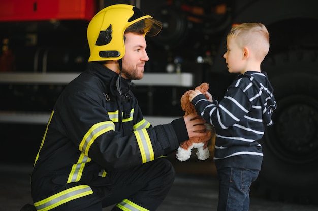 Vigile del fuoco sporco in uniforme che tiene il ragazzino salvato in piedi su sfondo nero