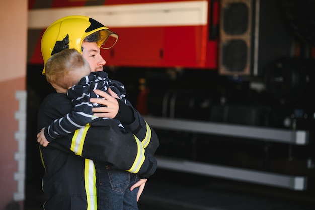 Vigile del fuoco sporco in uniforme che tiene il ragazzino salvato in piedi su sfondo nero