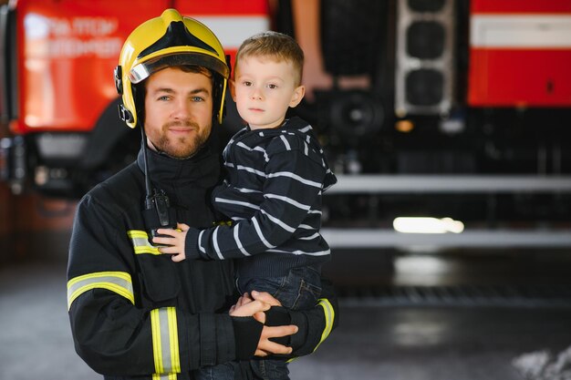 Vigile del fuoco sporco in uniforme che tiene il ragazzino salvato in piedi su sfondo nero