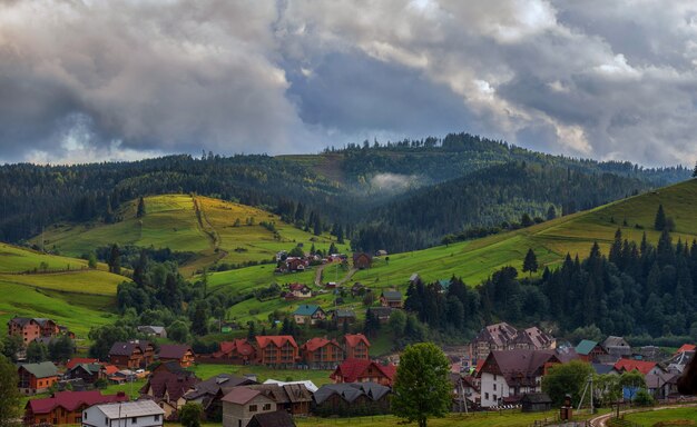 Villaggio di montagna, sullo sfondo di verdi pendii e foreste, cielo con nuvole temporalesche