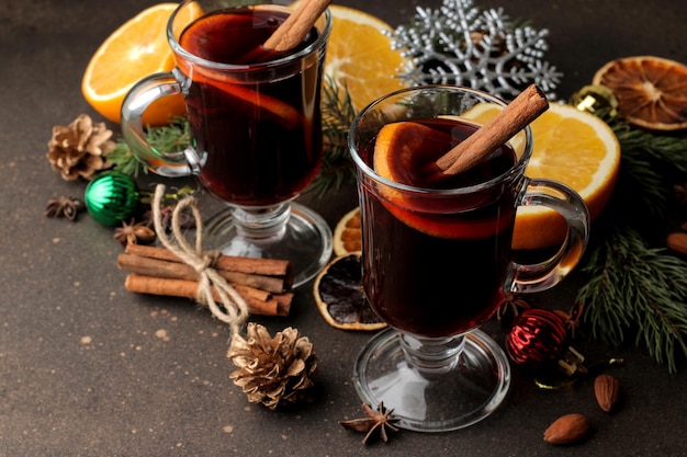 Vin brulé caldo con cannella e arancia in bicchieri di vetro e decorazioni natalizie su uno sfondo scuro. Natale. Capodanno.