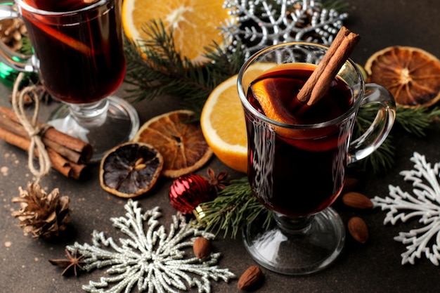 Vin brulé caldo con cannella e arancia in bicchieri di vetro e decorazioni natalizie su uno sfondo scuro. Natale. Capodanno.