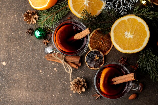 Vin brulé caldo con cannella e arancia in bicchieri di vetro e decorazioni natalizie su uno sfondo scuro. Vista dall'alto. Natale. Capodanno.