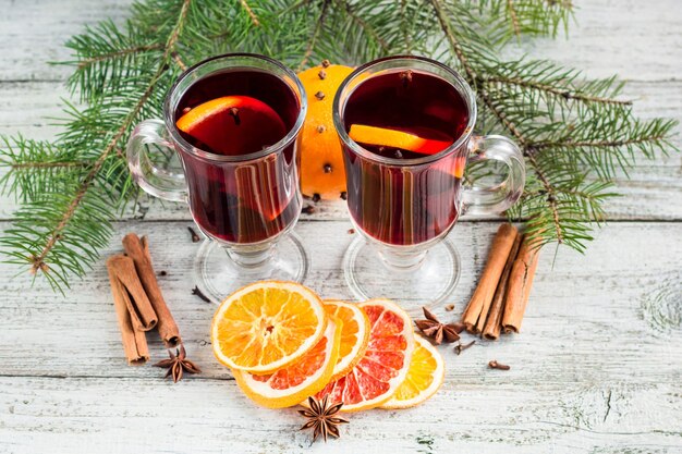 Vin brulé caldo di Natale con l'arancia e l'anice della cannella su fondo di legno bianco con l'albero