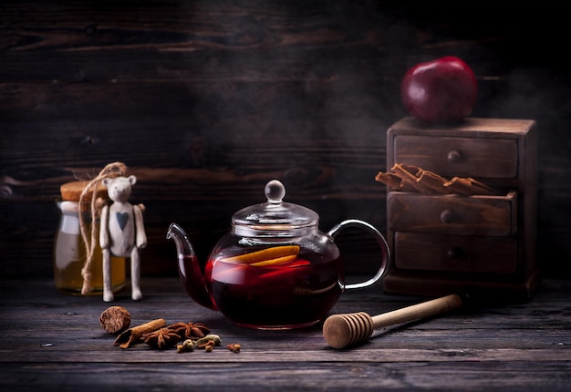 Vin brulé con spezie e miele in una teiera di vetro su un tavolo di legno. Bevanda calda natalizia invernale