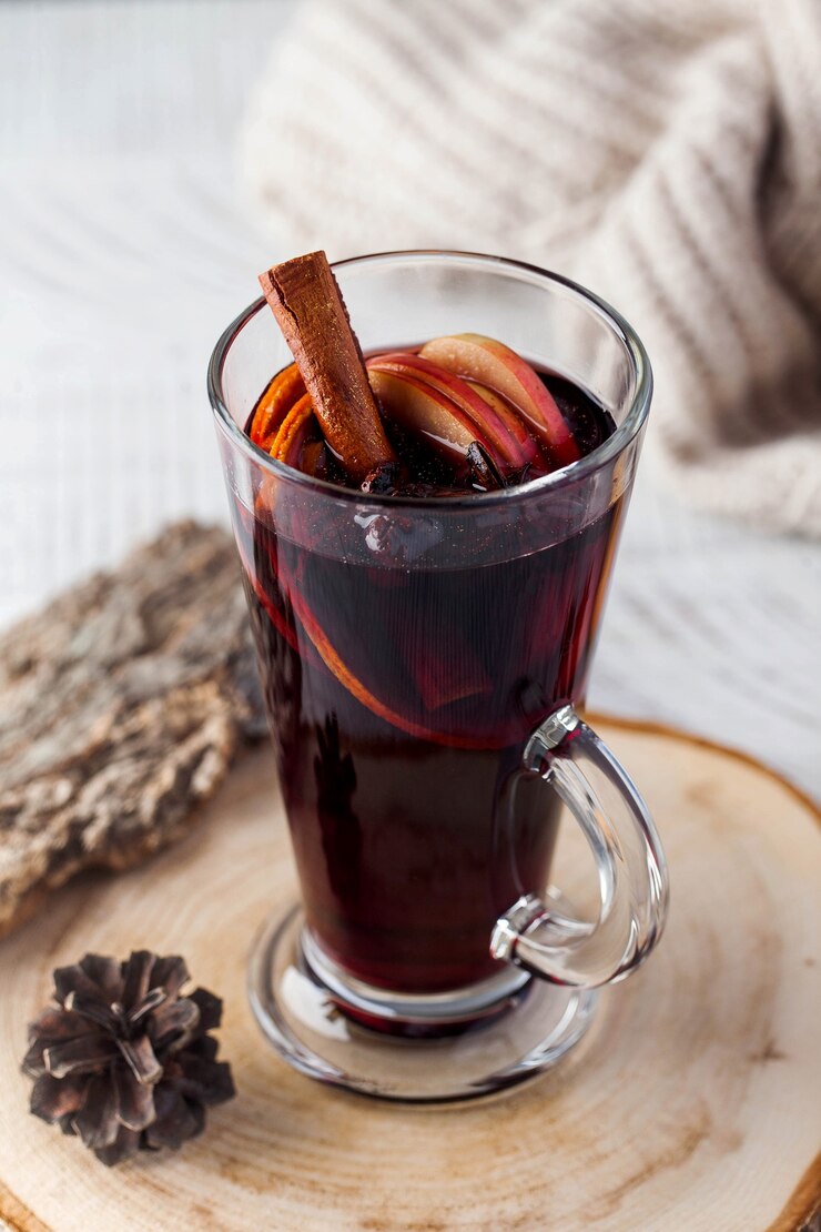 Vin brulé con una stecca di cannella, spezie in un bicchiere su un supporto di legno con una giacca di maglia in superficie