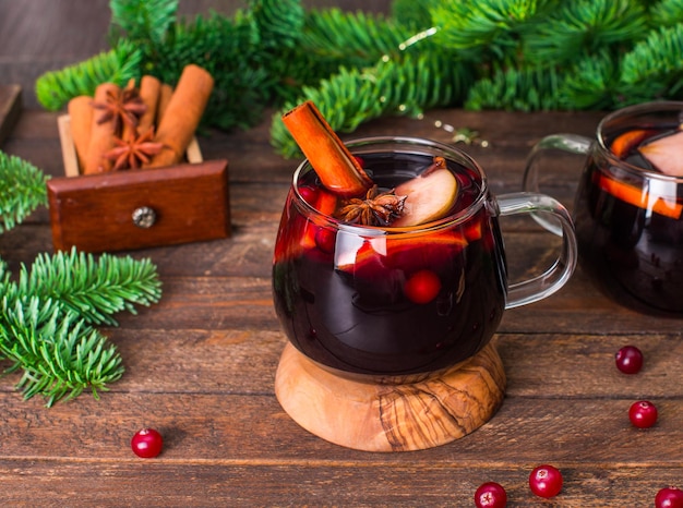 Vin brulé di Natale con mirtilli rossi di frutta e spezie in tazze di vetro su fondo di legno