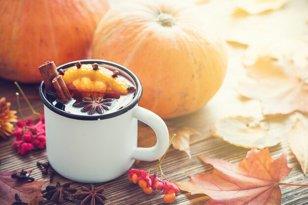 Vin brulé in tazza smaltata e zucche su tavola di legno con foglie autunnali