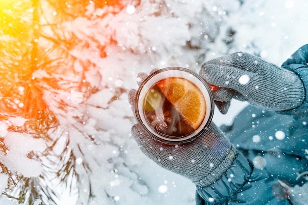 Vin brulé nelle mani di una ragazza durante una nevicata nella foresta di bevande calde invernali con aromi