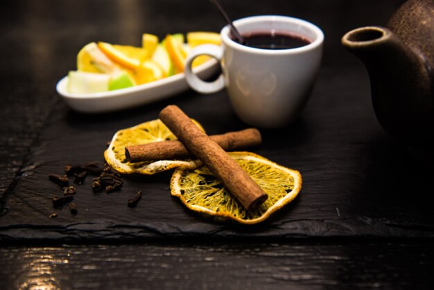 Vin brulè, sangria, vin brulè in una tazza bianca su un tavolo scuro, bancone bar con frutta, tè e spezie. Bastoncini di cannella e arancia