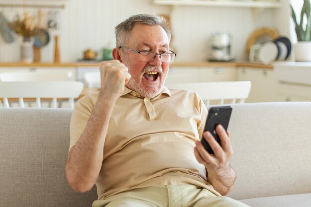 Vincitore euforico dell'uomo anziano di mezza età con il nonno maturo più anziano dello smartphone che guarda il cellulare phon