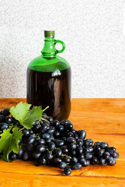 Vinificazione domestica Un enorme pennello di uve fresche succose scure sullo sfondo di una bottiglia di vino