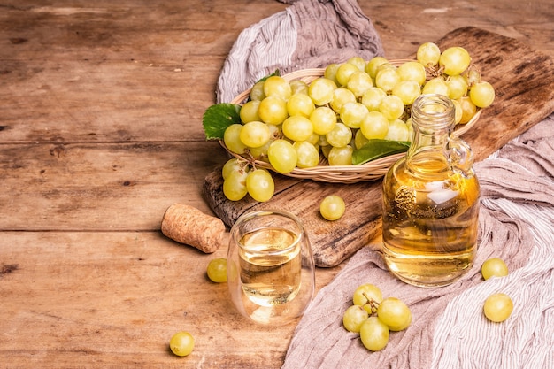 Vino bianco e uva in un cesto di vimini. Frutta fresca, vetro e bottiglia. Vecchie tavole di legno sfondo, copia spazio