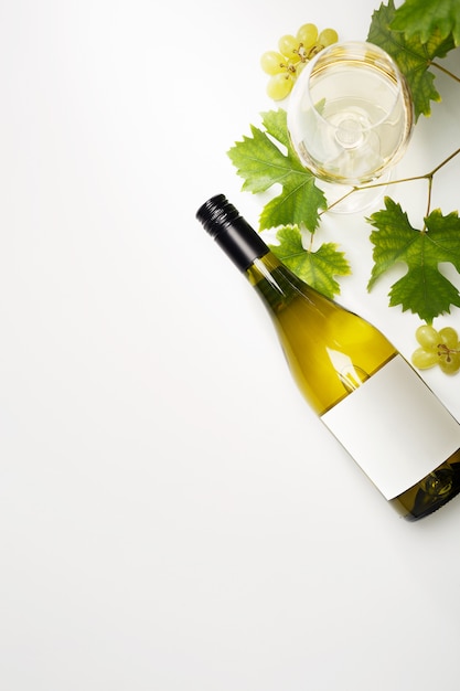Vino bianco in bicchieri, una bottiglia, uva e foglie di vite sul tavolo.