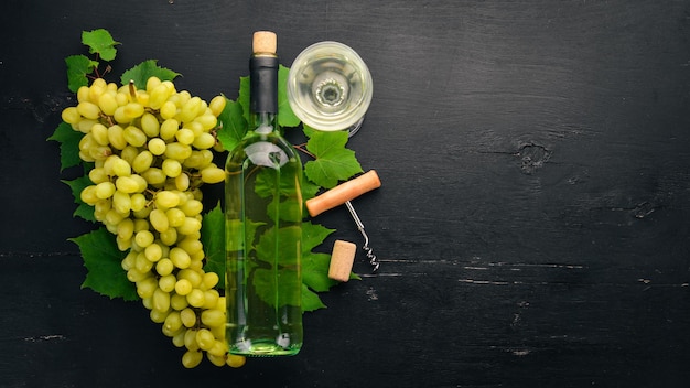 Vino bianco in una bottiglia con un bicchiere e uva su uno sfondo di legno nero Spazio libero per il testo Vista dall'alto