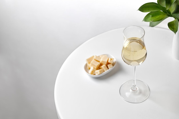 Vino bianco in vetro ricco su una tavola rotonda bianca con vaso di formaggio di verdure. Minimalismo. Elegante