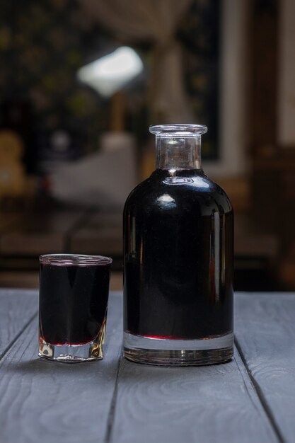 Vino o liquore aronia nero fatto in casa su superficie di legno nera