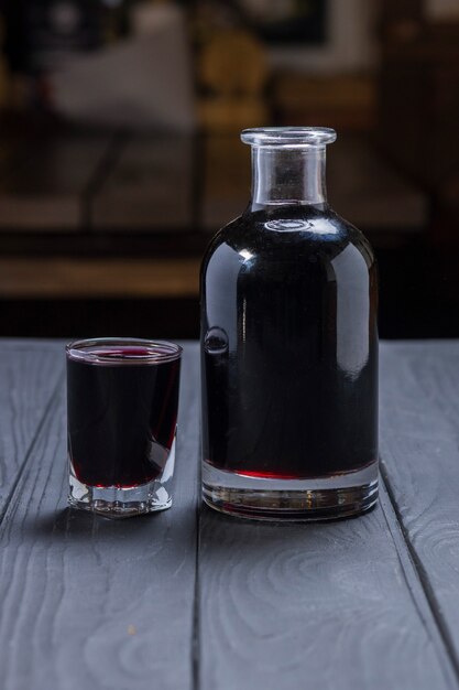 Vino o liquore aronia nero fatto in casa su superficie di legno nera