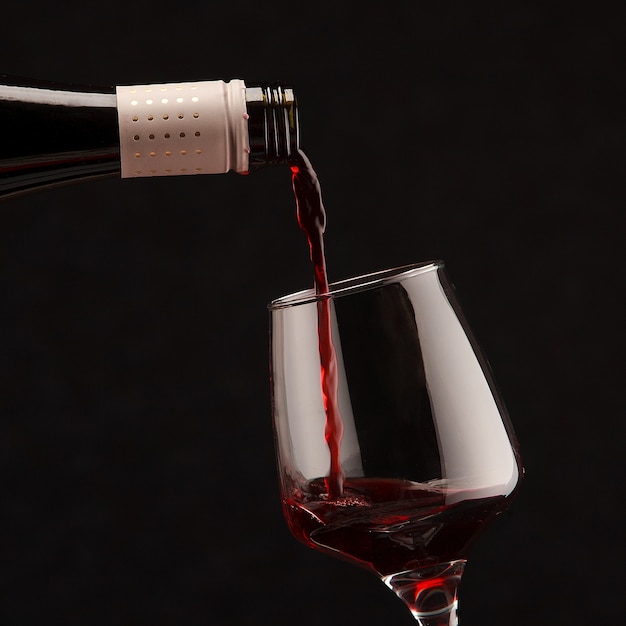 Vino rosso che versa nel bicchiere di vino su sfondo nero