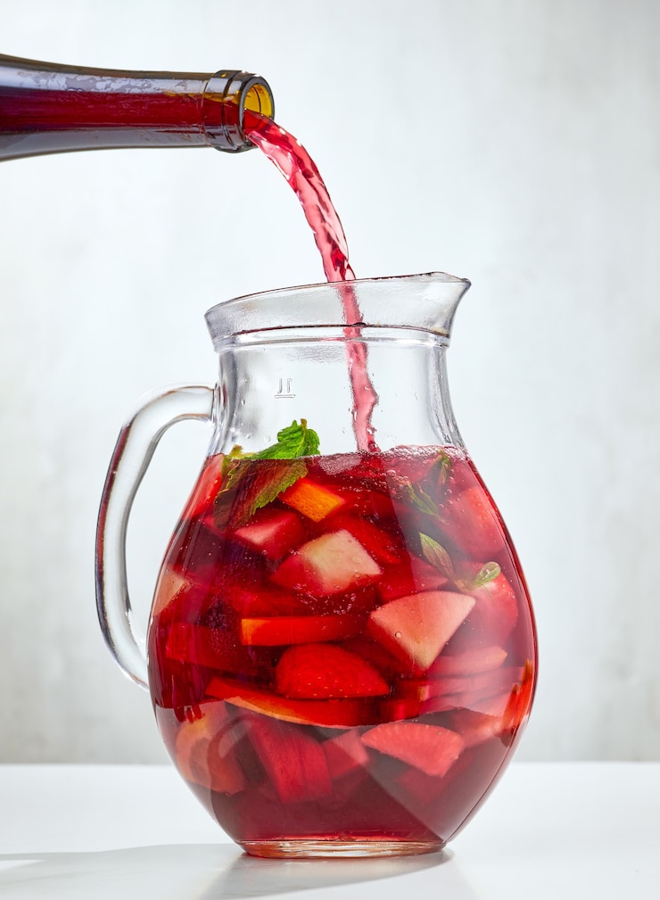Foto vino rosso che versa nella brocca di frutta tagliata. processo di preparazione della sangria rossa