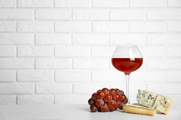 Vino rosso con uva e formaggio su sfondo muro di mattoni