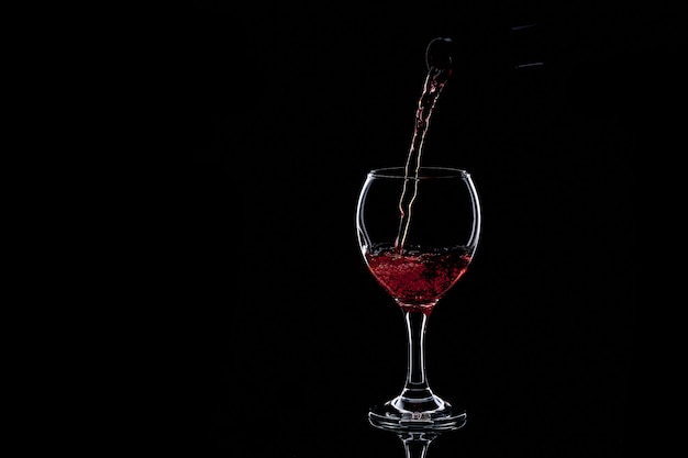 Vino rosso di versamento in vetro su oscurità. Silhouette isolata