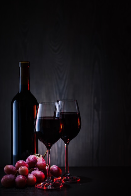 Vino rosso in bicchieri e bottiglia con grappolo d'uva rossa