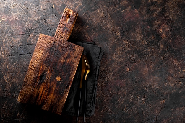 Vintage tagliere di legno tovagliolo di lino e posate su sfondo scuro arrugginito cibo sfondo
