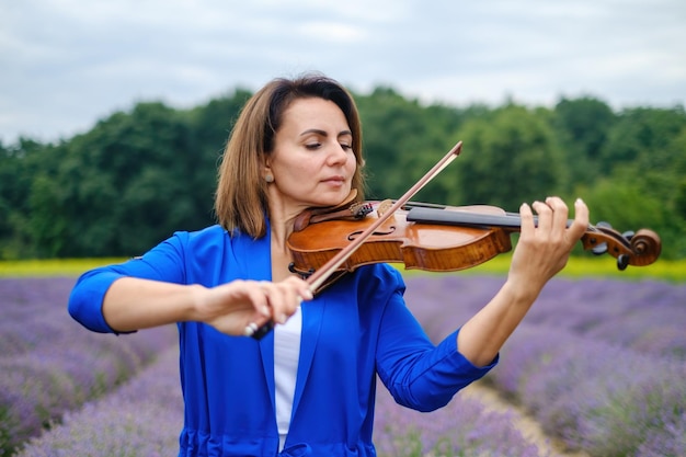 Violinistessa adulta che suona il violino in un campo di lavanda estivo