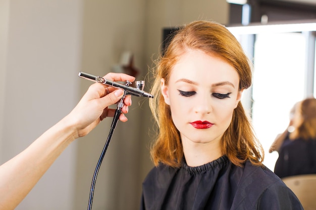 Visagiste che fa il trucco professionale della ragazza usando un aerografo. Un primo piano.