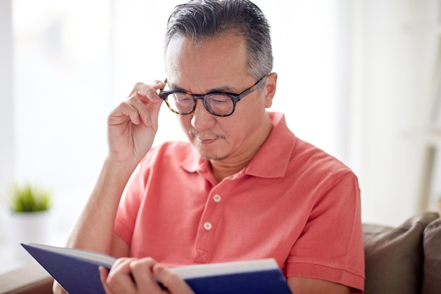 visione, tempo libero, letteratura e concetto di persone - uomo con gli occhiali seduto sul divano e leggere un libro a casa