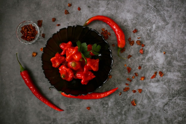 Visir di peperoncino rosso fermentato in un piatto nero e peperoncino fresco su una superficie grigia, vista dall'alto