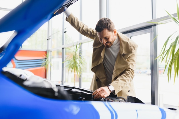 Visita concessionaria di auto. Bell'uomo barbuto sta accarezzando la sua nuova auto e sorridendo