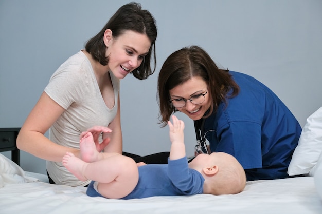 Visita del pediatra a casa della mamma e del bambino. Parlando dottoressa e giovane madre, bambino di 7 mesi sdraiato a casa sul letto dei genitori. La salute dei bambini fino a un anno